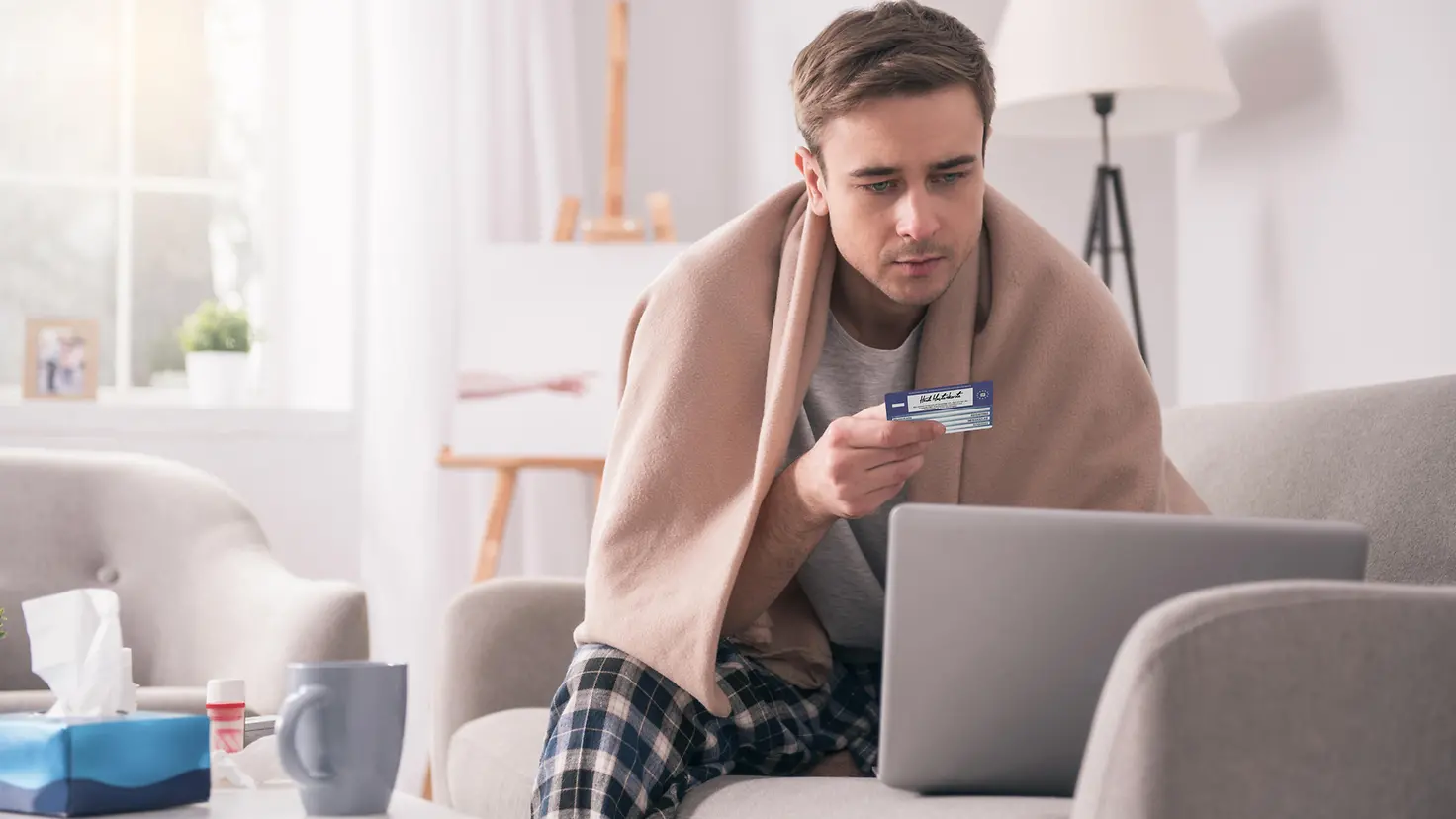 Kranker Mann vor dem Rechner, der seine Kreditkarte hält