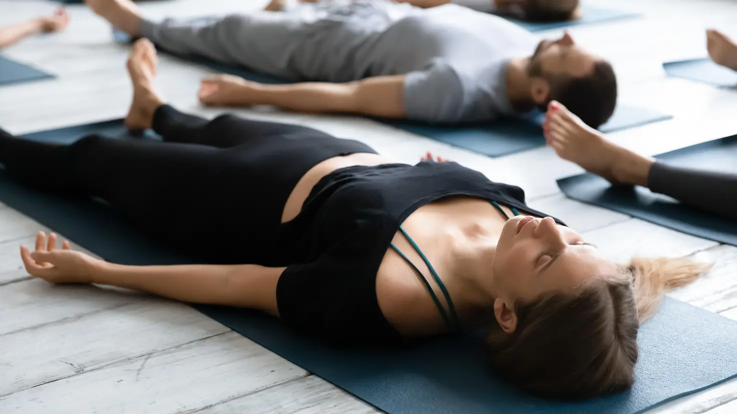 Zu sehen sind Menschen, die auf Yogamatten liegen und sich entspannen 