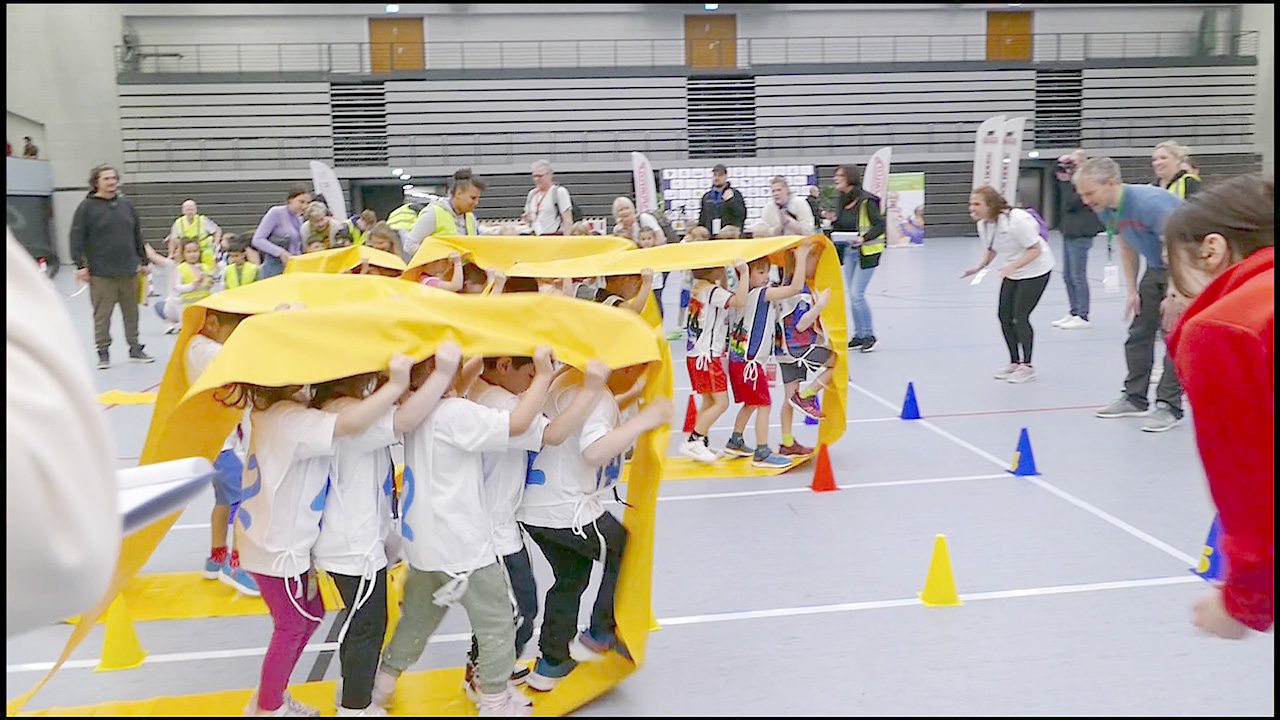 Kinder im Wettkampf versuchen, gemeinsam auf einem Plastikband schnell ins Ziel zu gelangen. 