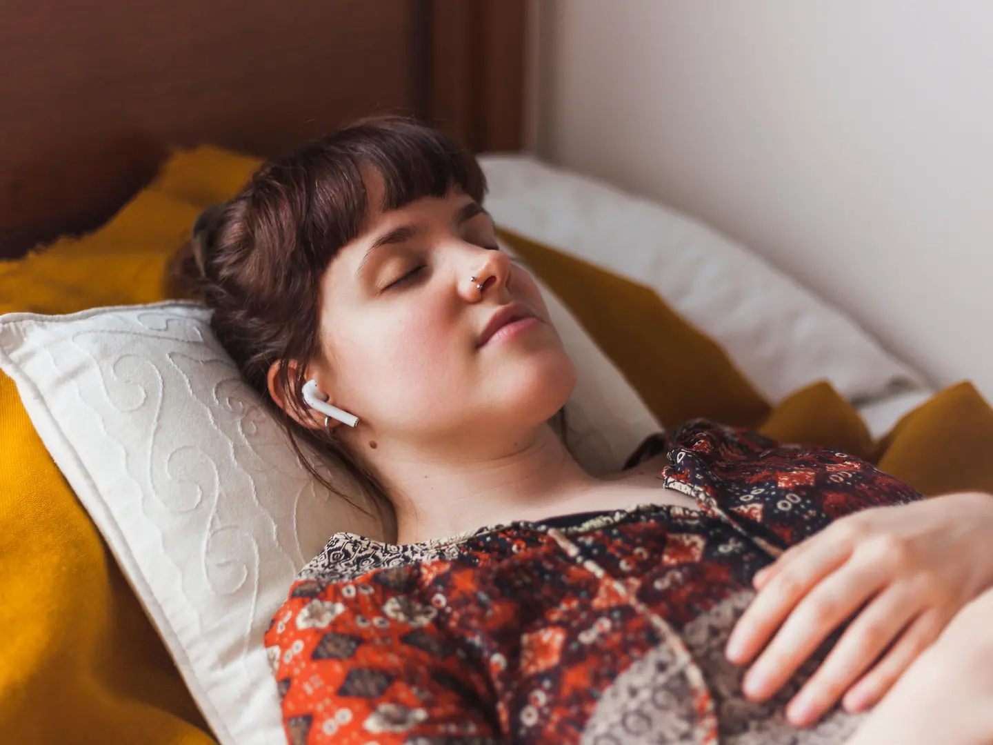 Eine junge Frau liegt schlafend mit Kopfhörern im Bett.