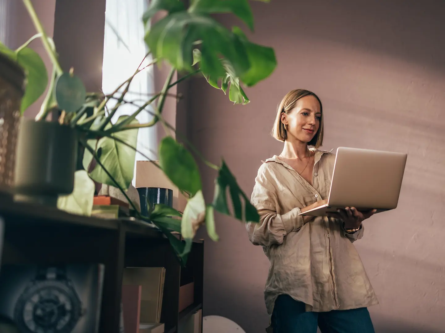 Junge Frau steht mit Laptop am Fenster.