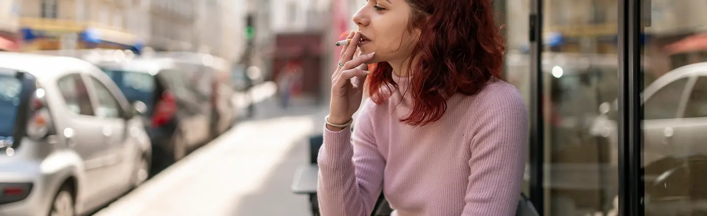 Eine junge Frau sitzt rauchend in einem Straßencafe.