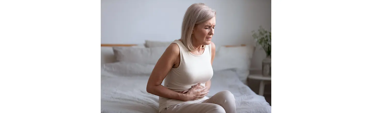 Eine Frau mit schmerzverzehrten Gesicht fasst sich an ihren Bauch.