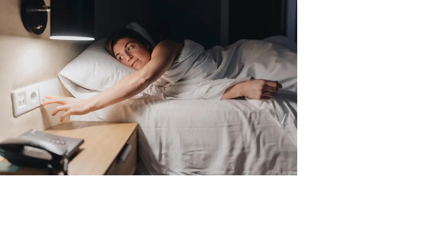 Eine junge Frau liegt im Bett und schaltet das Licht aus