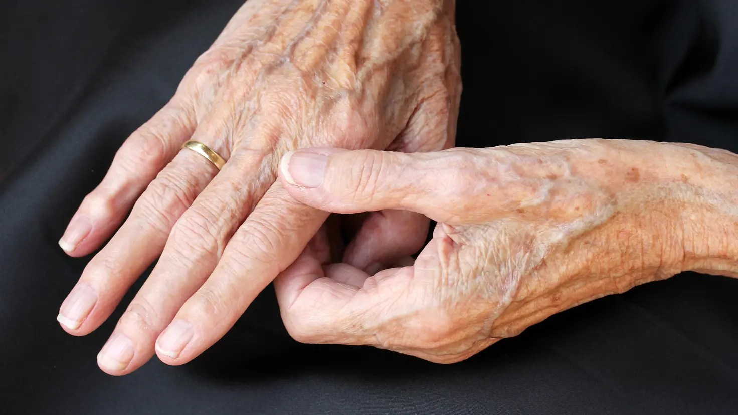 Zu sehen auf diesem Bild sind ein Paar Hände eines älteren Menschen. Der Zeigefinger der rechten Hand wird dabei durch einen Griff mit Daumen-Zeigefinger der linken Hand gehalten.