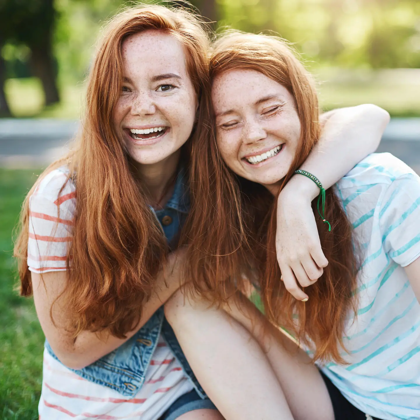Zu sehen auf diesem Bild ist ein weibliches Zwillingspaar mit roten Haaren. Die Mädchen lachen. 