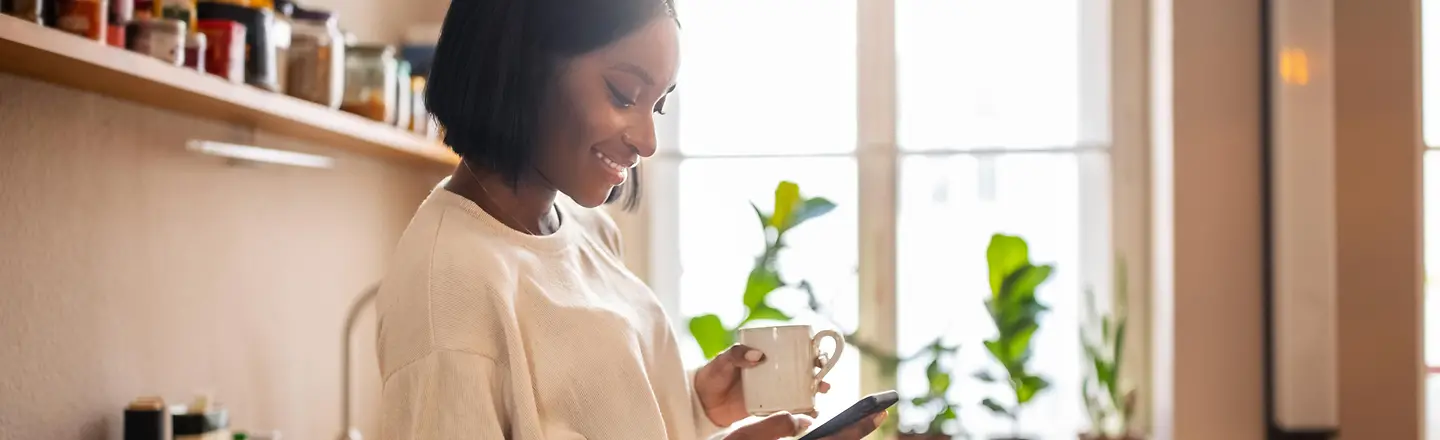 Eine junge Frau in der Küche nutzt ihr Smartphone