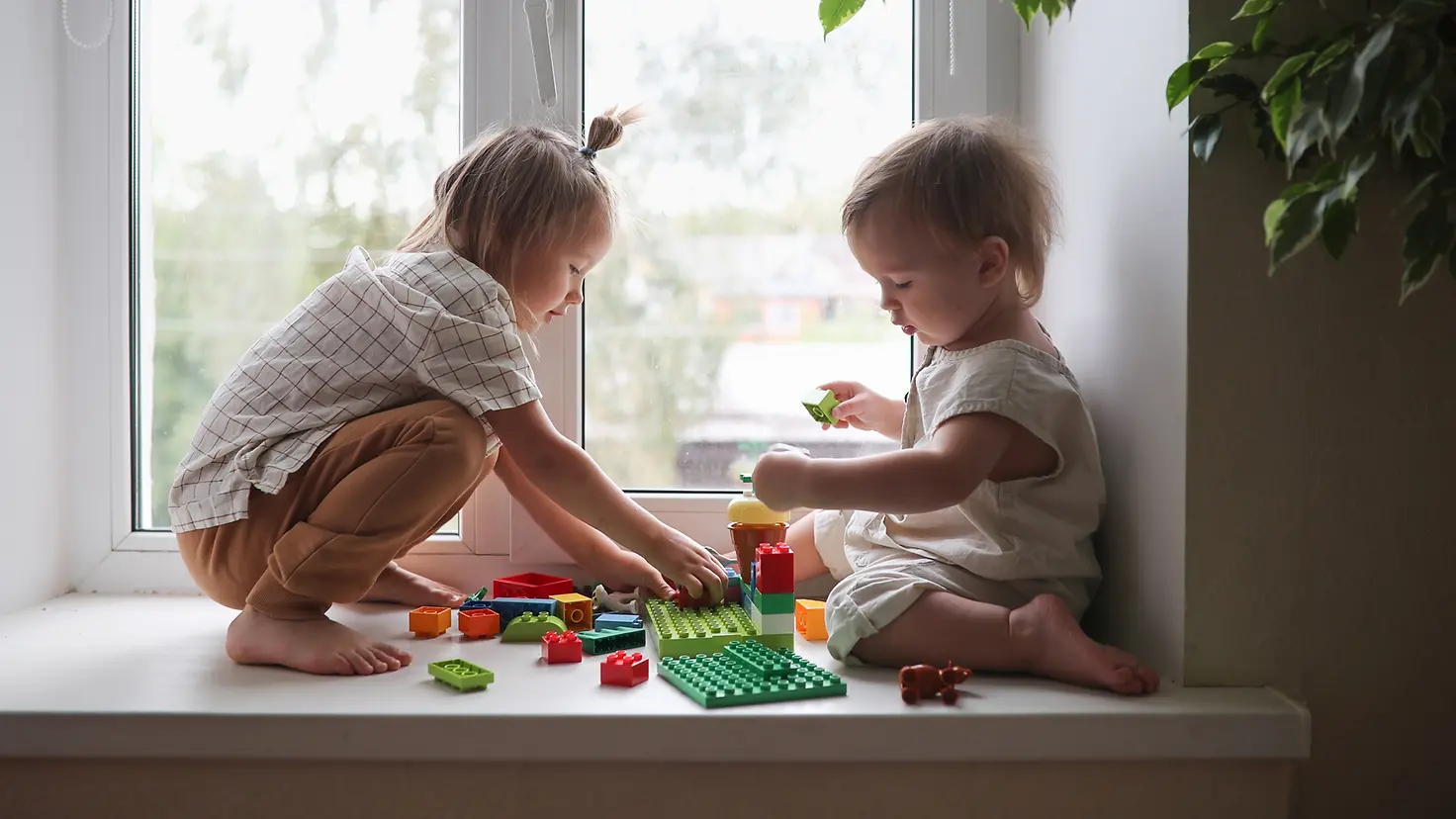 Zwei Kinder spielen auf einer Fensterbank mit Spielsteinen