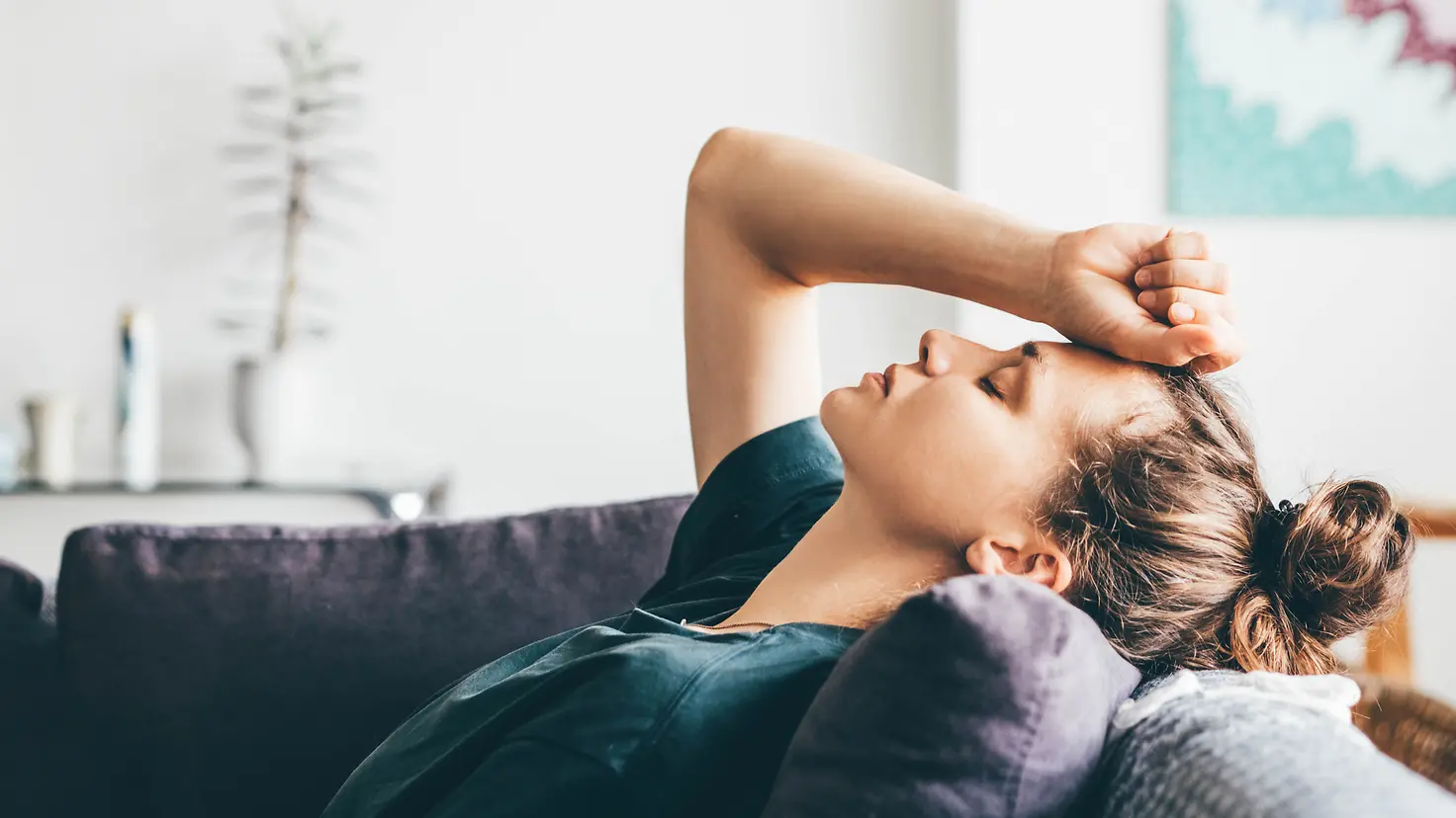 Eine junge Frau liegt mit Kopfschmerzen auf dem Sofa