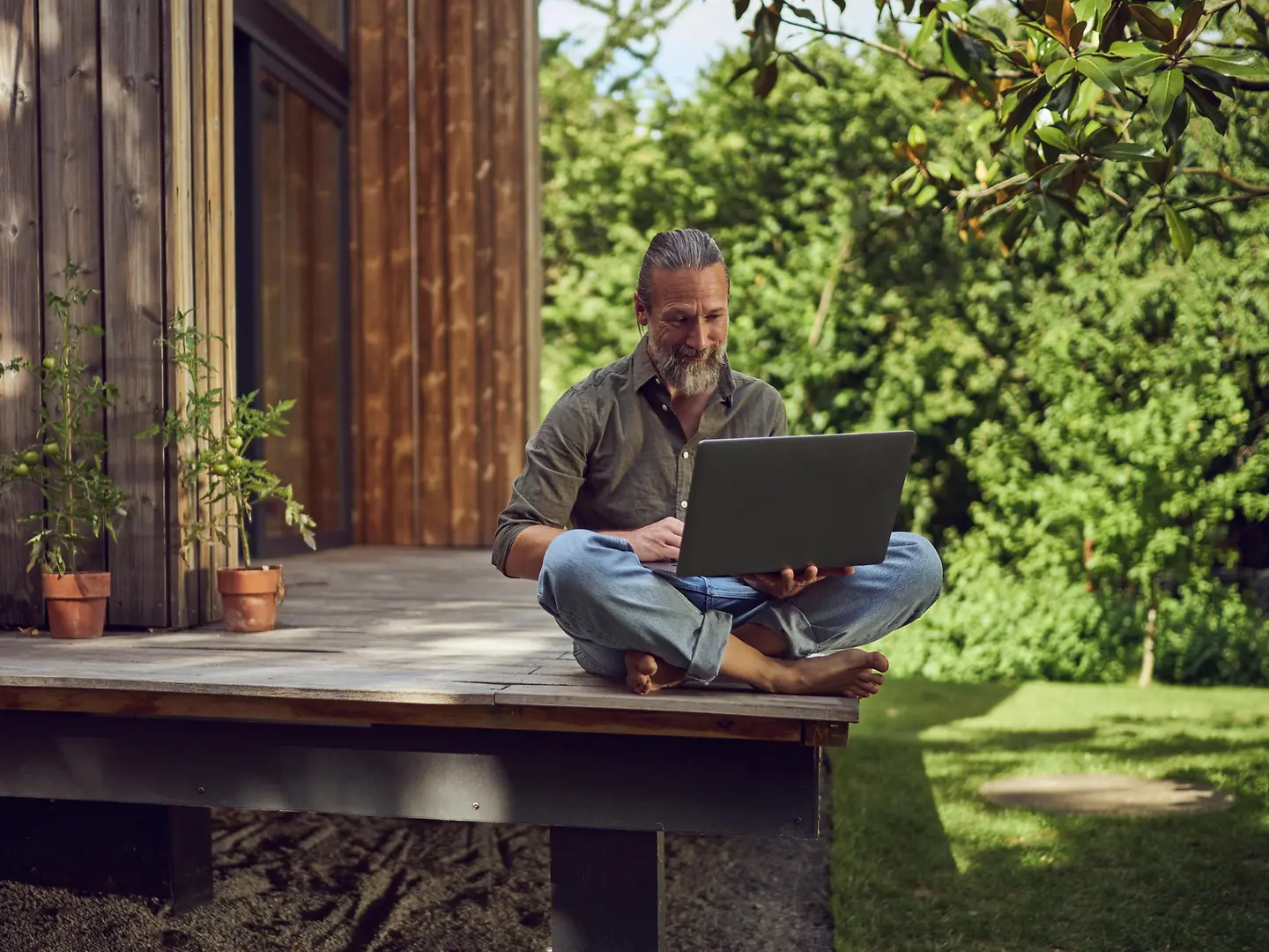 Mann sitzt auf Terasse mit Laptop auf dem Schoß