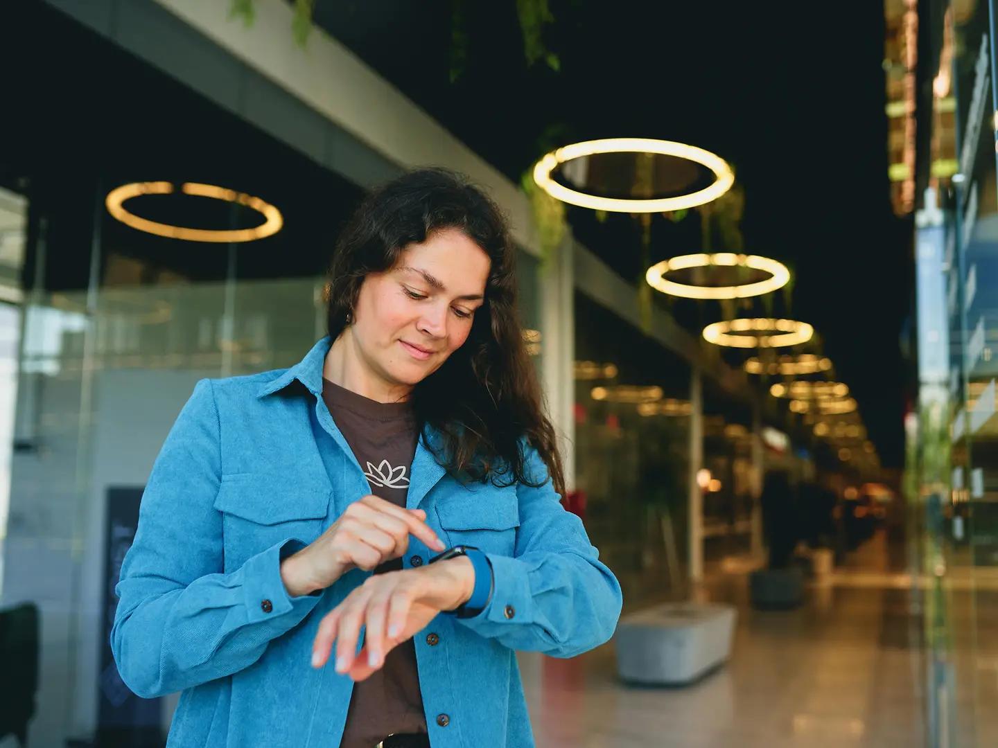 Eine Frau mit langen dunklen Haaren steht in einem modernen Innenraum und überprüft ihre Smartwatch