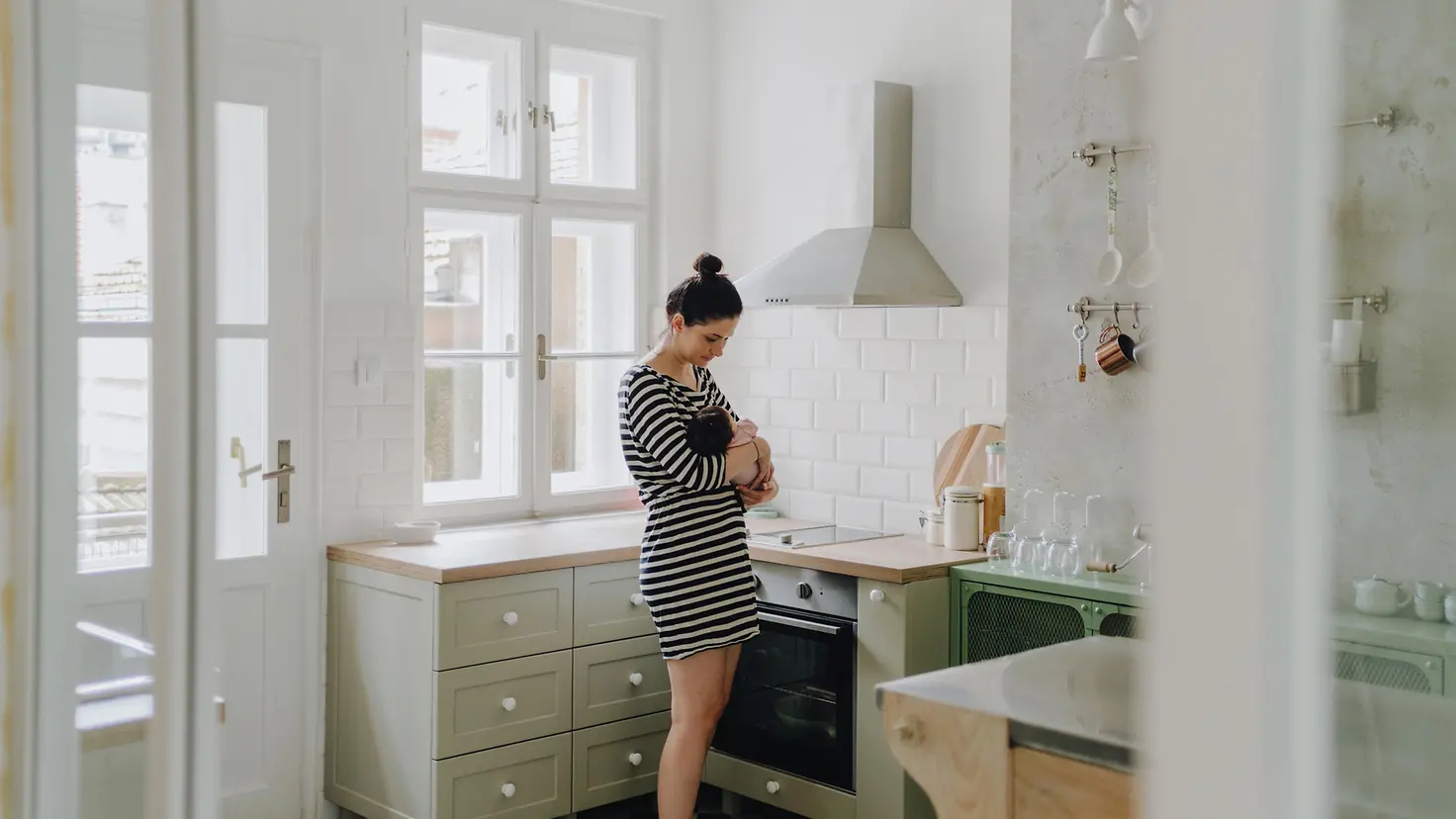 Eine Frau steht in einer Küche und hält ein neugeborenes Baby