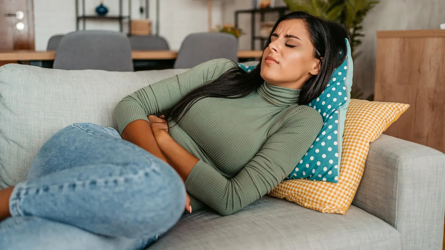 Eine junge Frau liegt mit Bauchschmerzen auf dem Sofa