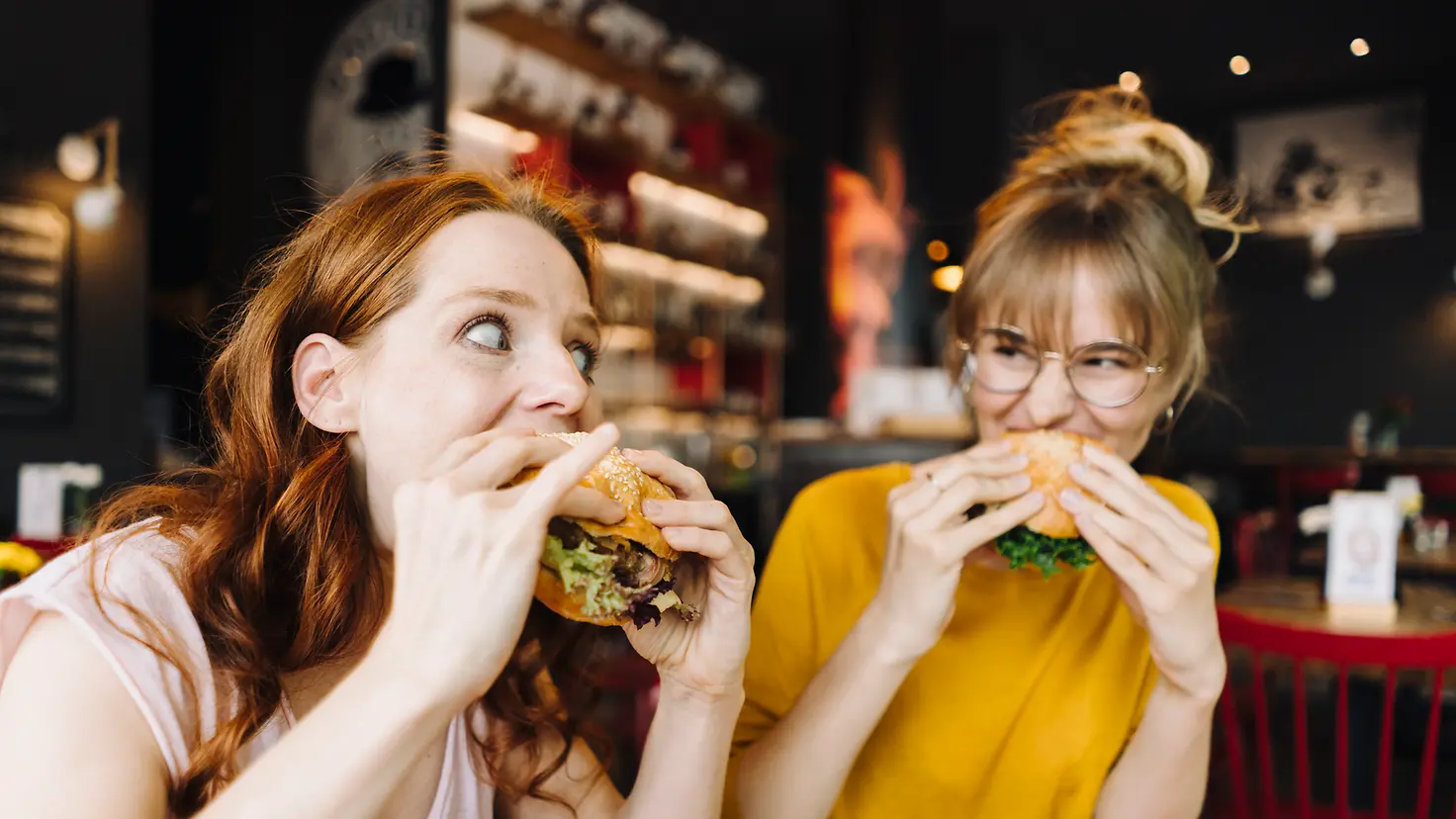 Zwei junge Frauen sitzen in einem Restaurant und essen genüsslich Burger