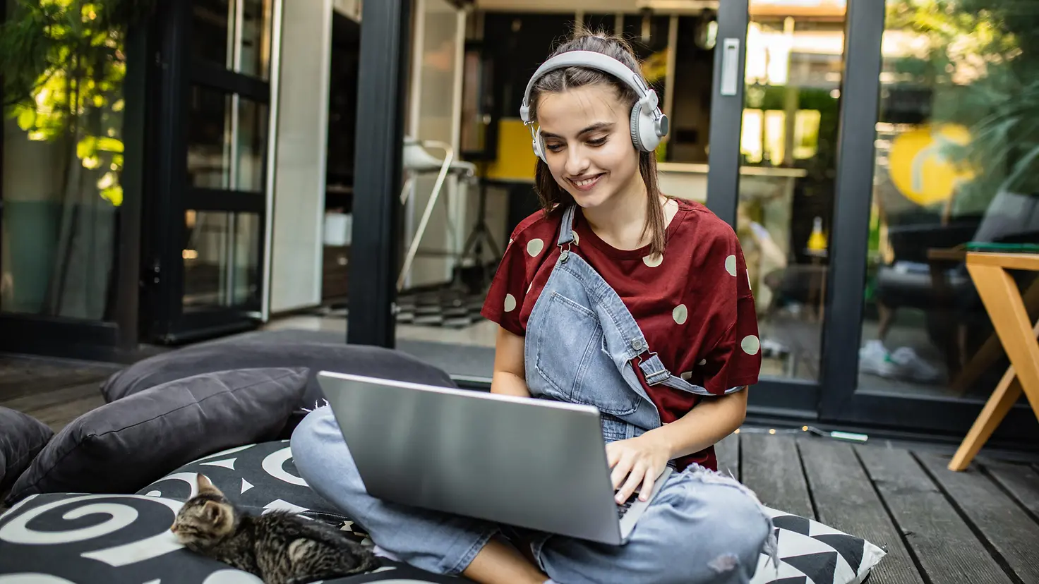 Eine junge Frau mit Kopfhörer arbeitet zuhause an ihrem Laptop